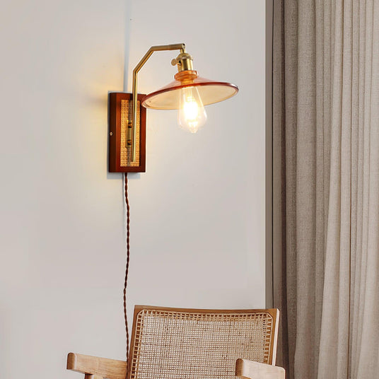 The sconce lit above a cane chair beside a curtain, its cord hanging down