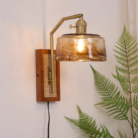 The amber drum shade lit beside a fern, the walnut plate and cord below