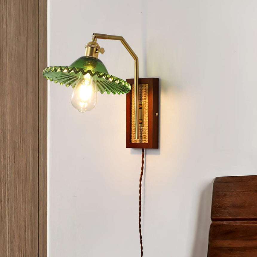 The green ruffled glass shade lit on a pale wall beside a wood chair