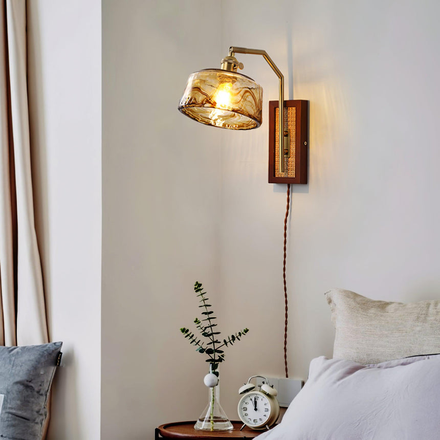 The sconce with an amber drum shade above a nightstand with a clock beside a bed