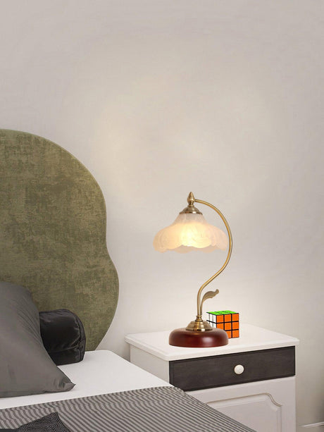 Flower shade lamp lit on a nightstand beside a made bed