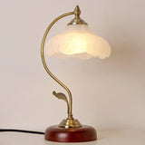 Flower shade lamp lit warm against a pale wall, seen up close