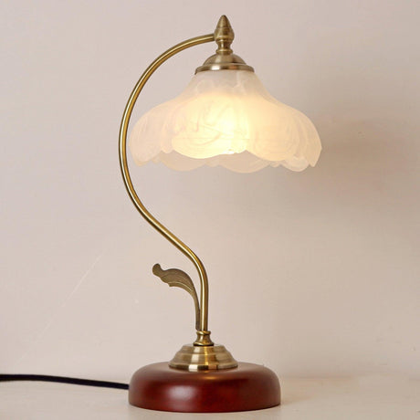 Flower shade lamp lit warm against a pale wall, seen up close