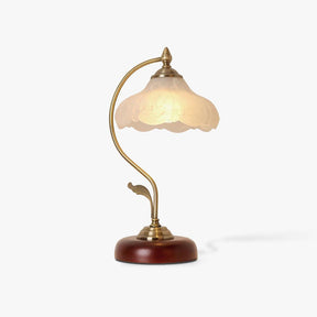 Table lamp with a frosted flower glass shade on a curved brass arm