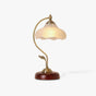 Table lamp with a frosted flower glass shade on a curved brass arm