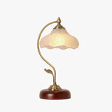 Frosted flower shade lamp lit on a plain ground, the arm curving over