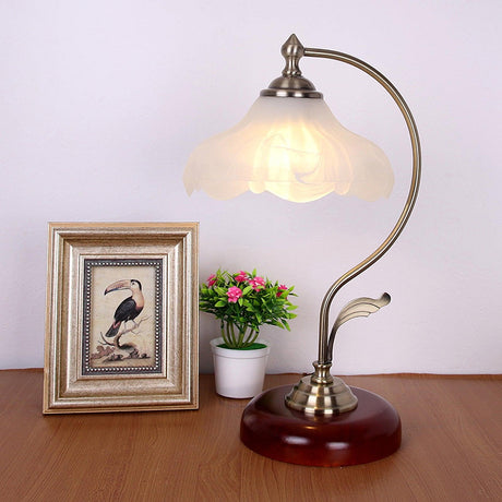 Flower shade lamp lit on a desk beside a framed bird print