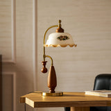 Antique brass table lamp lit on a wood desk against a pale wall