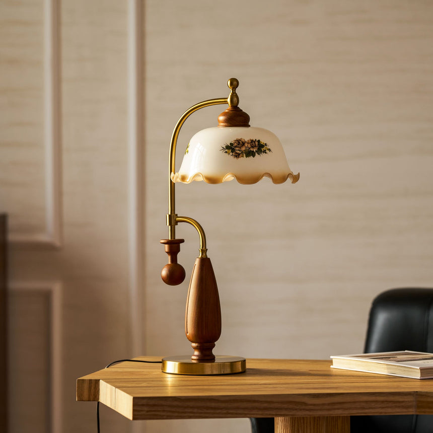 Antique brass table lamp lit on a wood desk against a pale wall