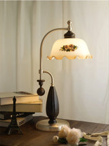 Antique brass table lamp lit on a desk beside books and a globe