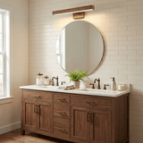 Brass bar lit above a round mirror over a wood vanity on a white brick wall