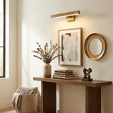 Brass bar lit above a framed print and a round mirror over a walnut console