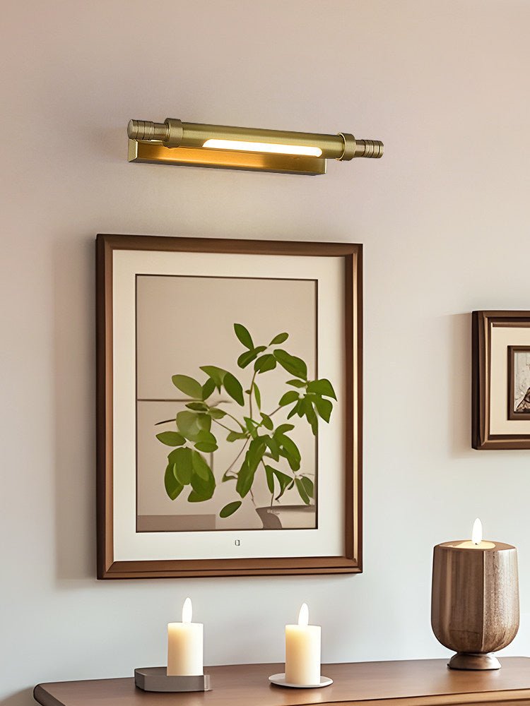 Brass tube lit over a pair of framed prints above a dark wood dresser