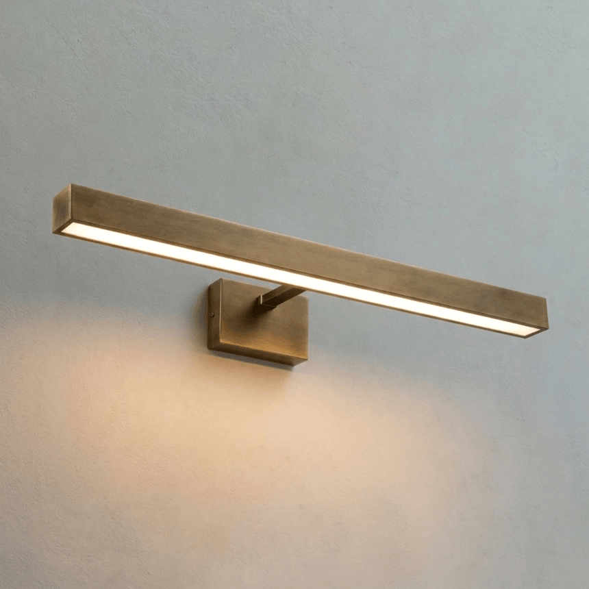 The longest brass bar lit on a pale wall, light running the length of its face