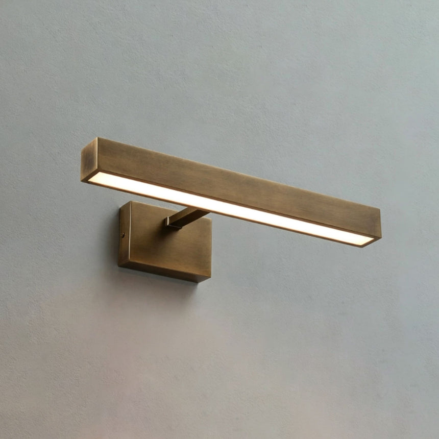 The shortest brass bar lit on a pale wall, the block bracket under its middle