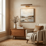Brass bar lit above a framed canvas on a walnut sideboard beside an armchair