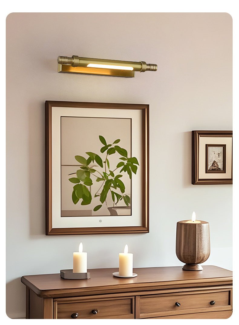 Brass tube lit over framed prints above a wood dresser with candles