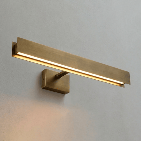 The longest brass bar lit on a pale wall, the block bracket at its middle