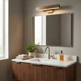Brass bar lit above a rectangular mirror over a walnut vanity with a plant