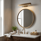 Brass bar lit above a round brass mirror over a basin beside a tall window