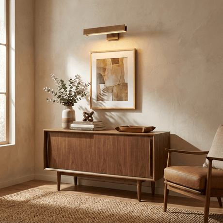 Brass bar lit above a framed print on a walnut sideboard with flowers and a chair