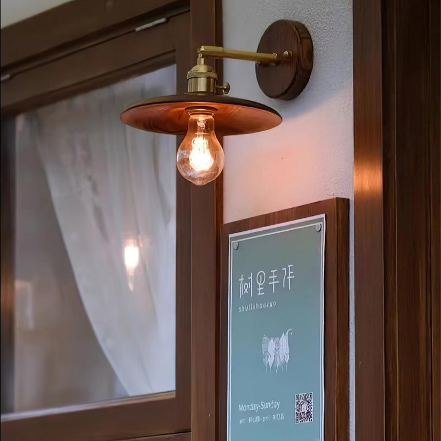 Brass and walnut sconce lit beside a window frame with a curtain