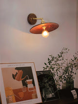 Brass and walnut sconce lit in a hallway beside framed pictures