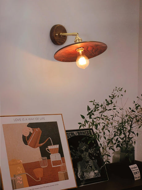 Brass and walnut sconce lit in a hallway beside framed pictures
