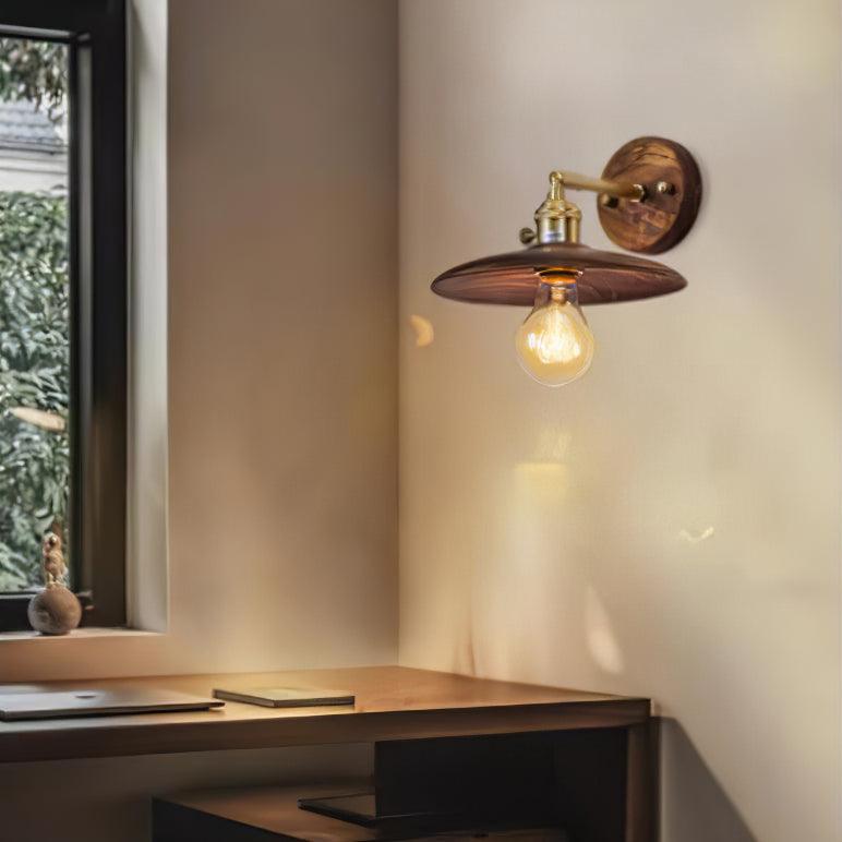 Sconce lit on the wall above a wood desk beside a window