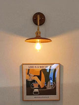 Brass and walnut sconce lit above a small framed print on a pale wall