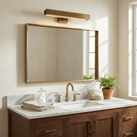Brass bar lit above a wide framed mirror over a walnut vanity with a plant