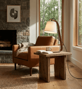 Arc lamp lit on a side table beside a leather armchair and a fireplace