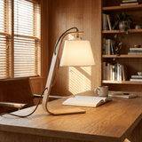 Arc lamp lit on a wood desk beside a notebook and a cup