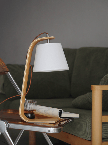 Arc lamp lit on a table beside an open magazine and a green sofa