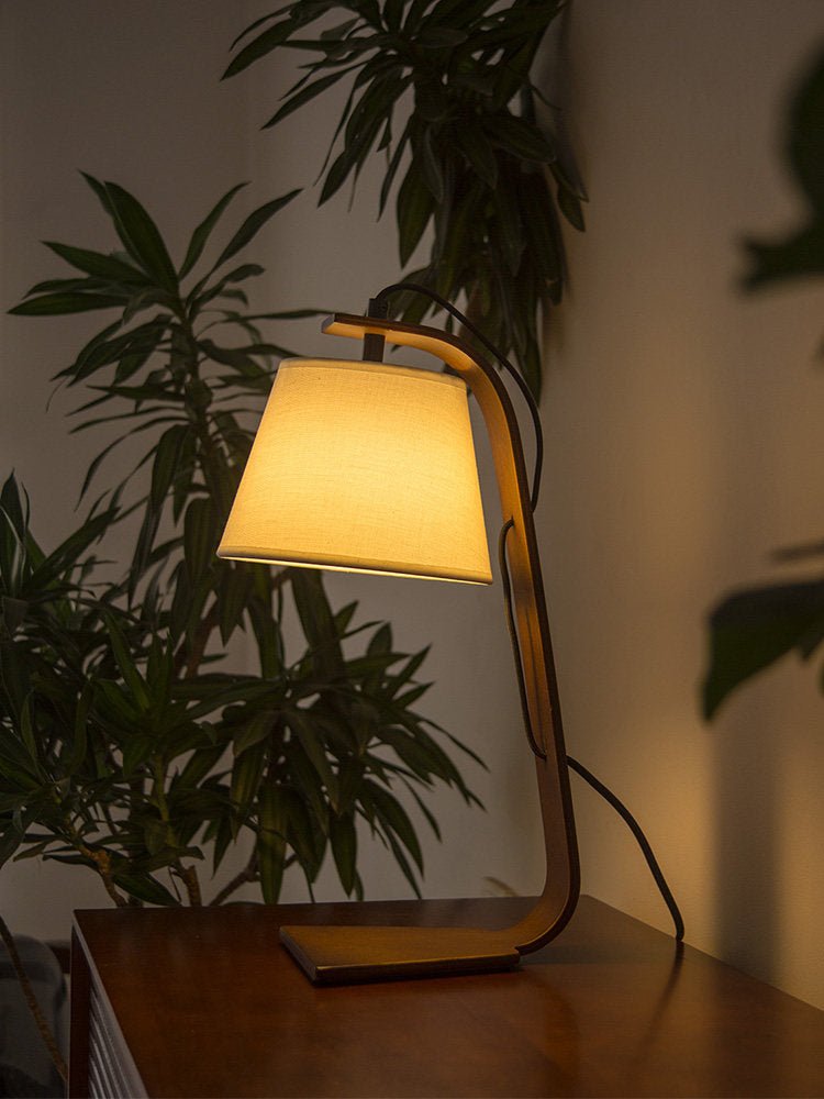 Arc lamp lit on a dark table beside a tall green plant