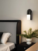 Black arch lit beside a bed with a plant on the nightstand below it