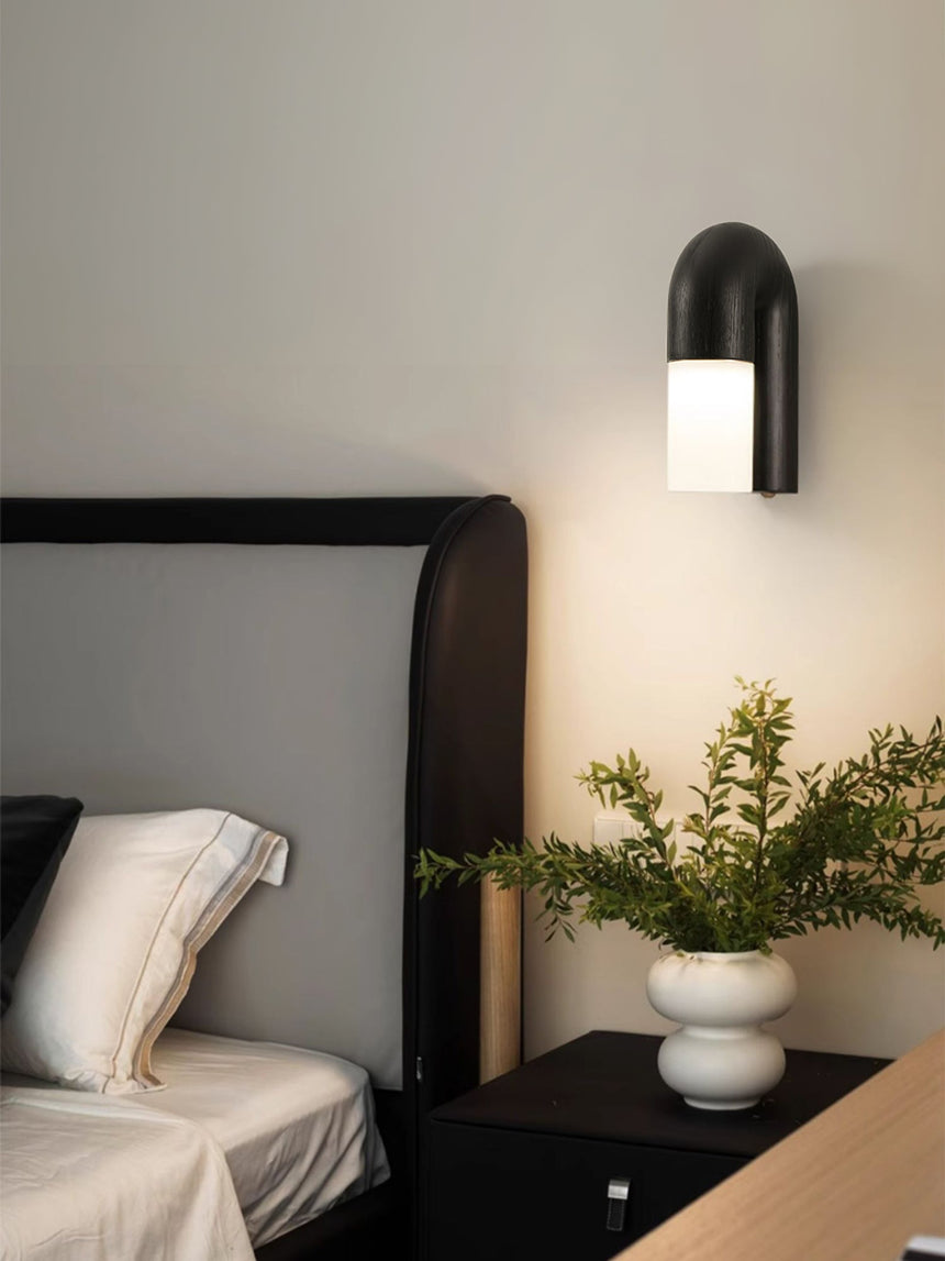 Black arch lit beside a bed with a plant on the nightstand below it