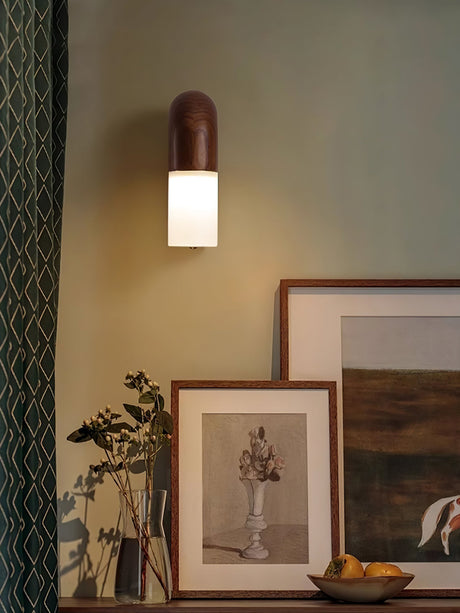 Sconce lit above framed prints leaning on a console beside a plant