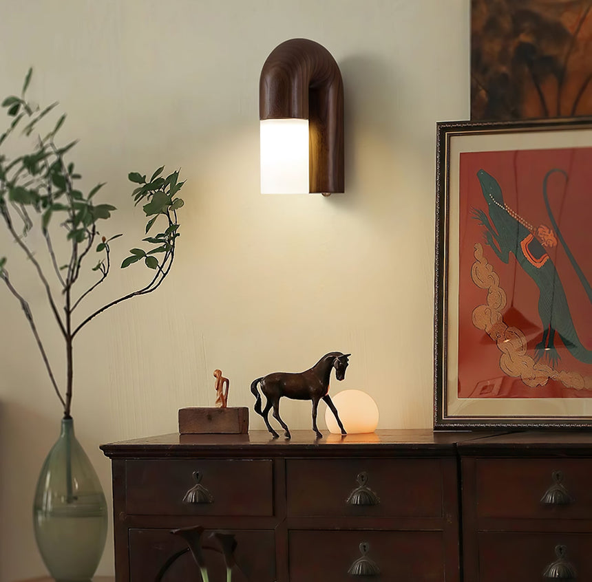 Sconce lit above a sideboard with a vase of branches and framed prints