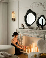 The sconce lit beside a stone mantel with candles and round mirrors