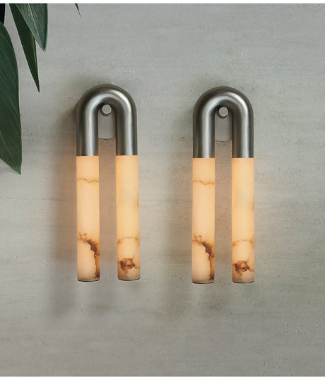 A pair of nickel sconces lit side by side on a pale stone wall