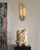 The sconce beside a stone sculpture on a plinth in front of a painting