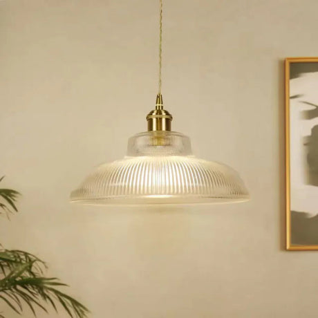 Clear prismatic shade hanging in front of a framed print on a pale wall