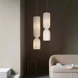 Two tall pleated pendants beside a sofa in a dark room