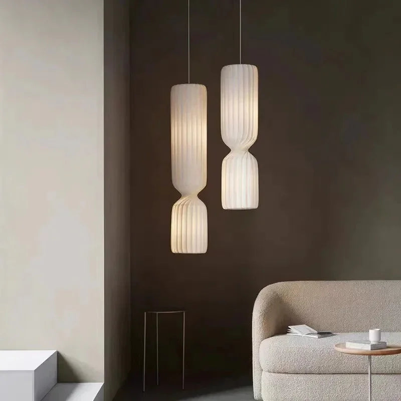 Two tall pleated pendants beside a sofa in a dark room