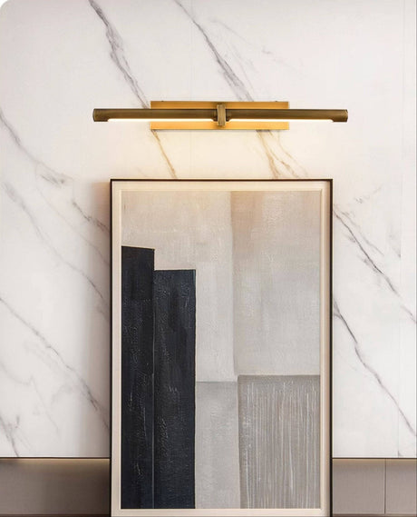 Brass twin bar lit over framed artworks leaning against a marble wall