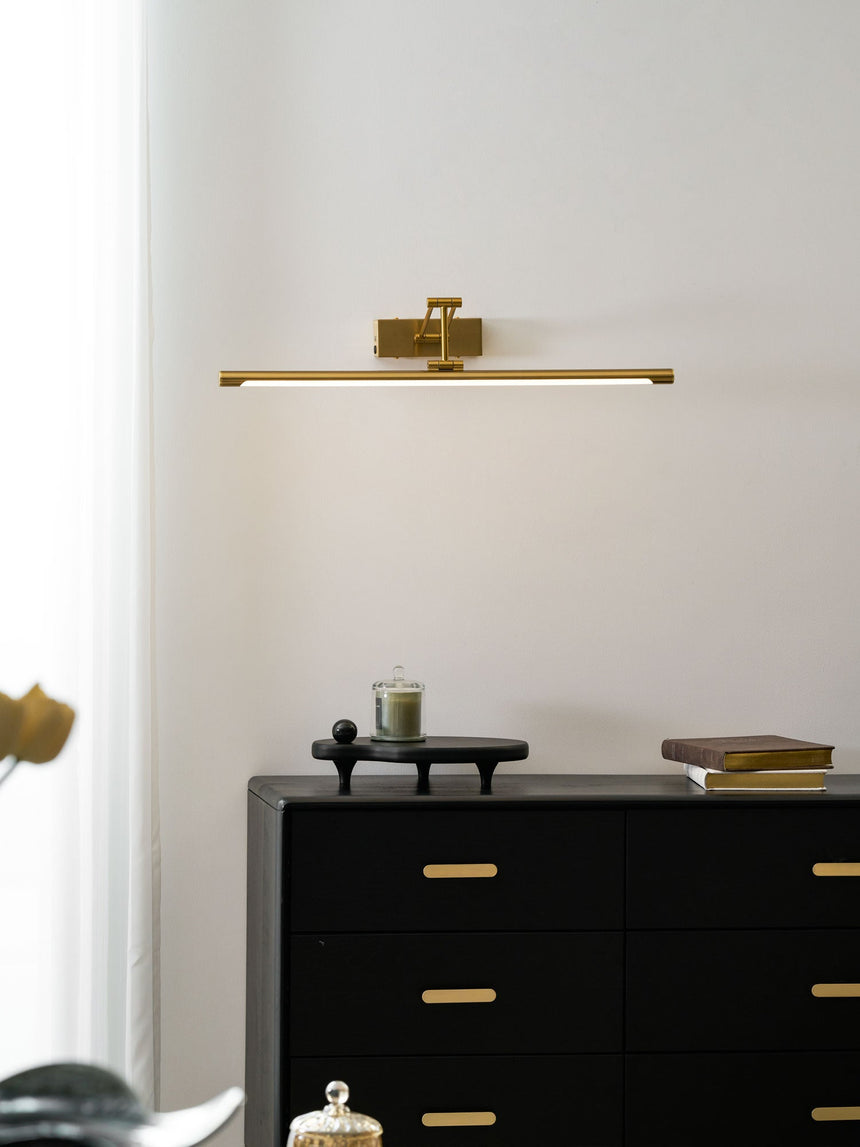 Lit above a black chest of drawers holding books and a small brass sculpture