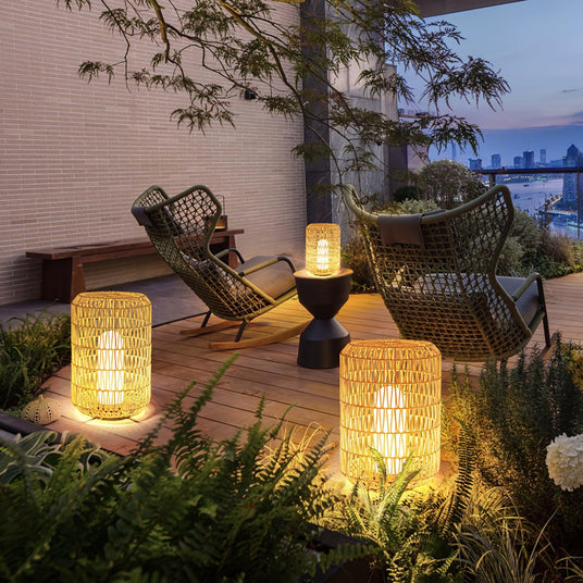 Lanterns lit on a timber deck beside woven chairs and garden planting