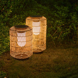 Two lanterns lit on a lawn against a dark hedge in an evening garden