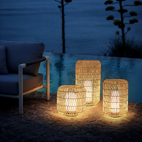 Four lanterns lit on gravel beside a pool and an outdoor sofa at dusk